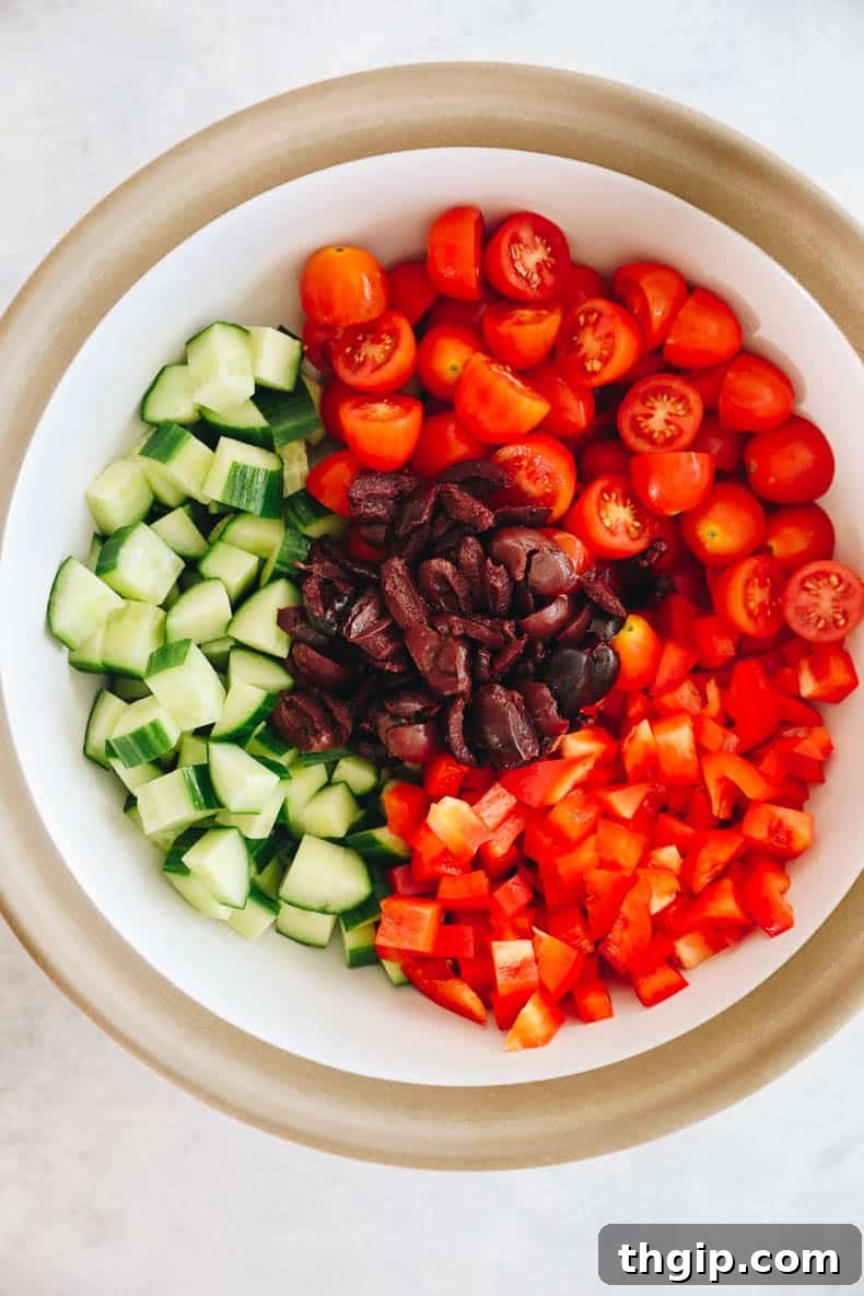 Mediterranean Pasta Delight 4 cherry tomatoes, cucumber, olives and bell pepper in a white and brown bowl, ready to be mixed.
