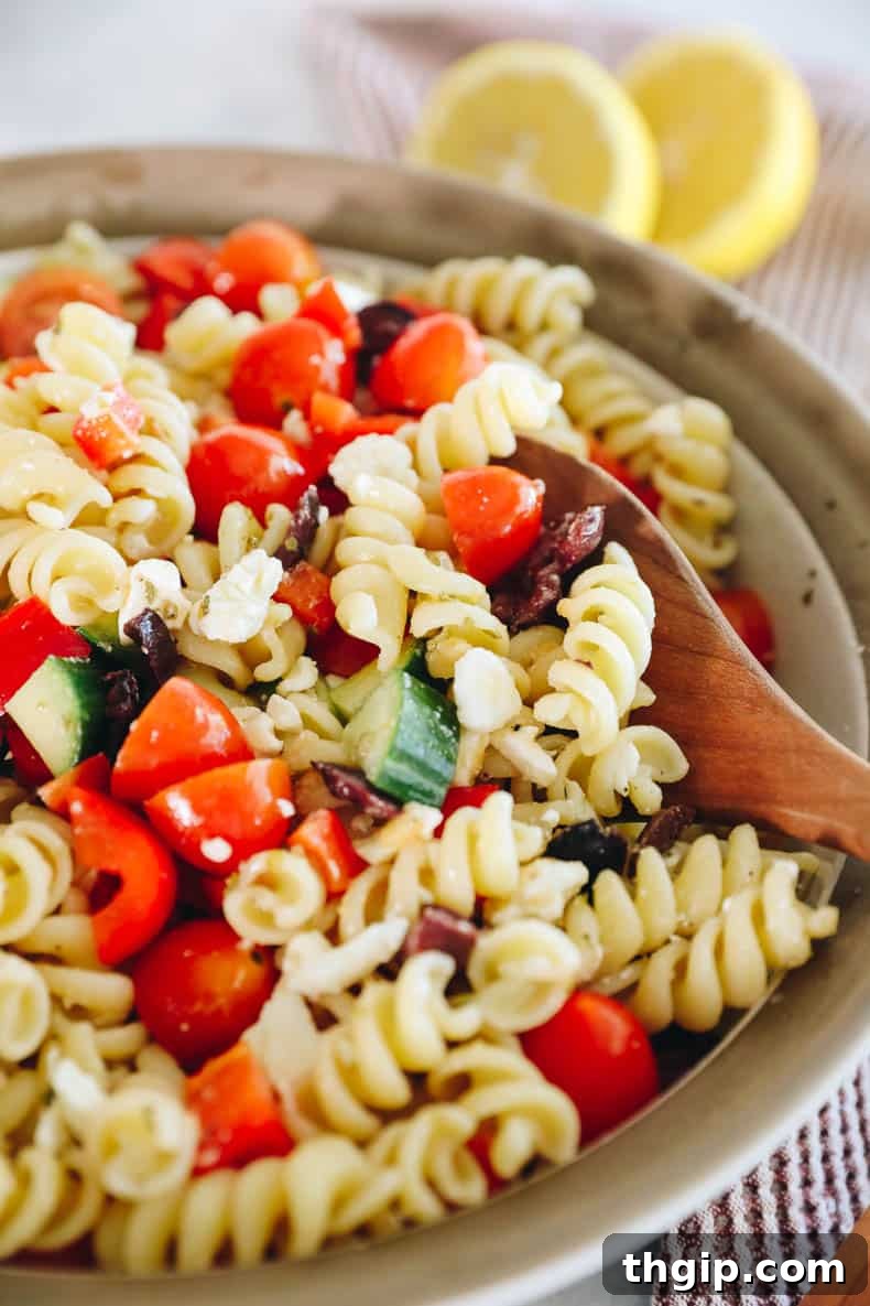 Mediterranean Pasta Delight 6 A wooden spoon scooping up a generous portion of Greek pasta salad from a large bowl, showcasing the fresh ingredients.
