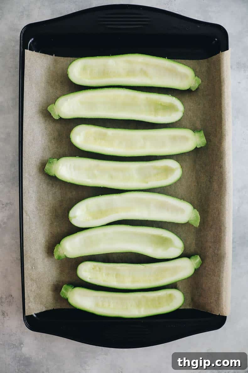 Zucchini halves with seeds scooped out, creating small wells on a parchment-lined baking sheet, ready for toppings.