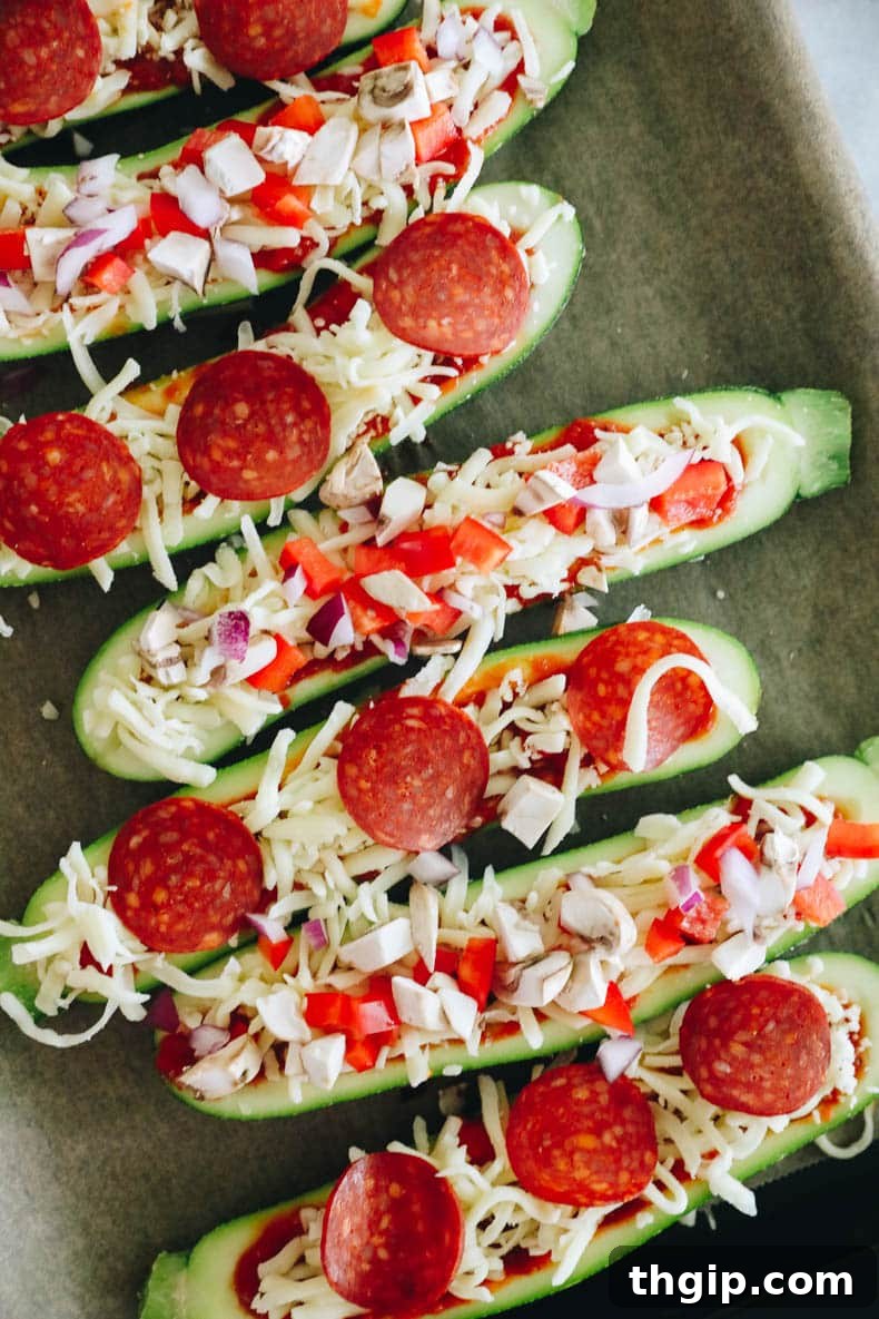 Assembled zucchini pizza boats on a baking sheet, topped with sauce, cheese, and various ingredients like pepperoni and vegetables, ready for baking.