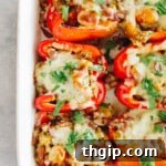 Vegetarian quinoa stuffed peppers with melted cheese and sprinkled cilantro on top, on a white plate.