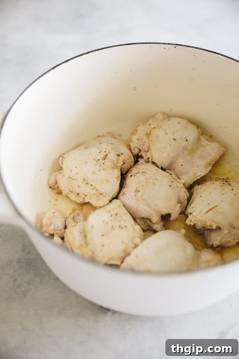 Chicken thighs browning in a large stock pot, developing a rich, golden crust.