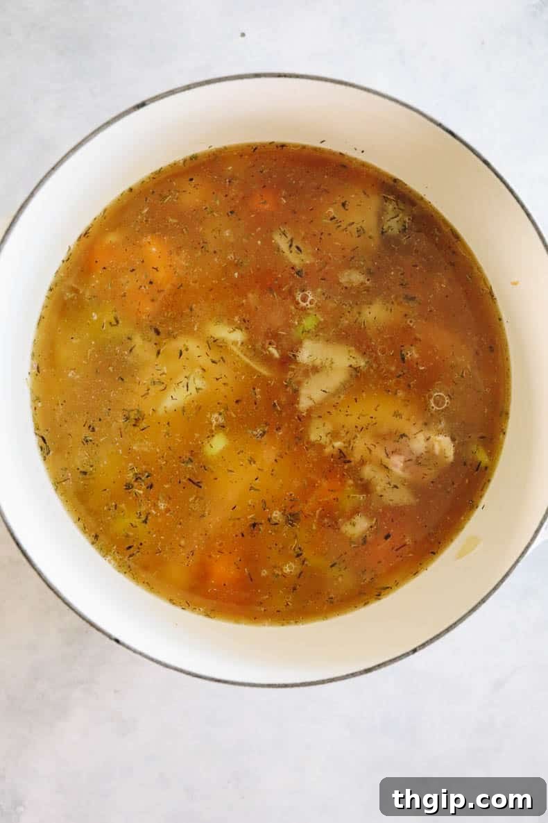 Chicken and vegetables simmering in savory broth in a large pot, infusing flavors.