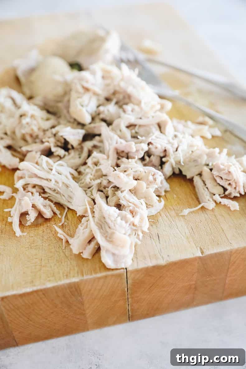 Shredded boneless skinless chicken thighs on a cutting board, ready to be added back to the soup.