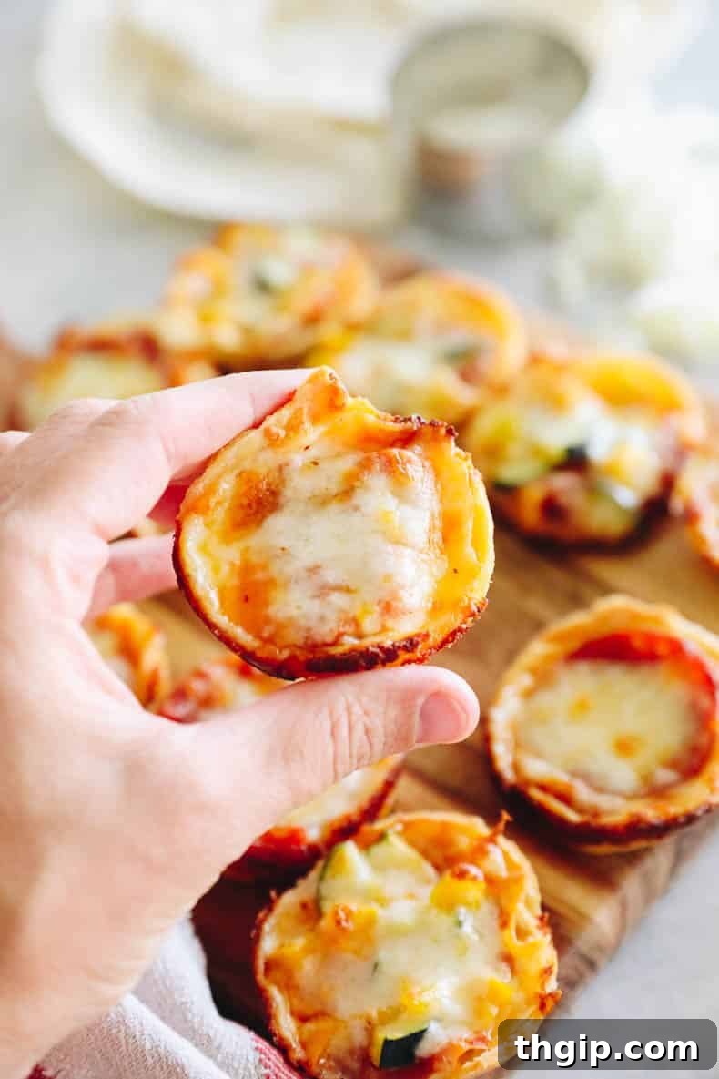 A hand holds a single mini tortilla pizza, showing the melted cheese, visible pepperoni, and crispy golden tortilla base.