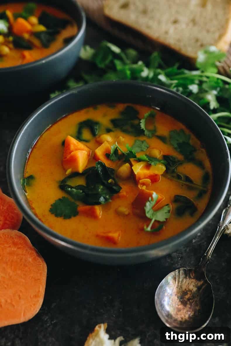 A vibrant bowl of curried sweet potato soup, garnished with garbanzo beans, fresh swiss chard, and aromatic cilantro, ready to be enjoyed.