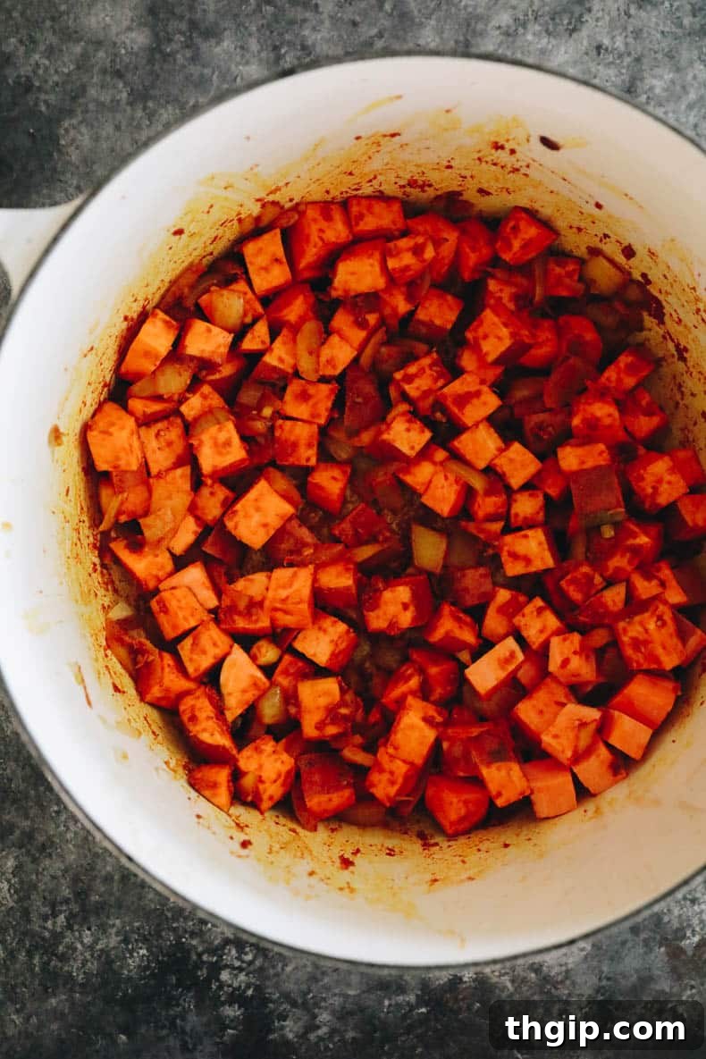 Cubed sweet potatoes coated with aromatic spices in a large stock pot, ready for simmering.