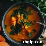 A vibrant bowl of curried sweet potato soup with chopped sweet potatoes, chickpeas and swiss chard, ready to be served.