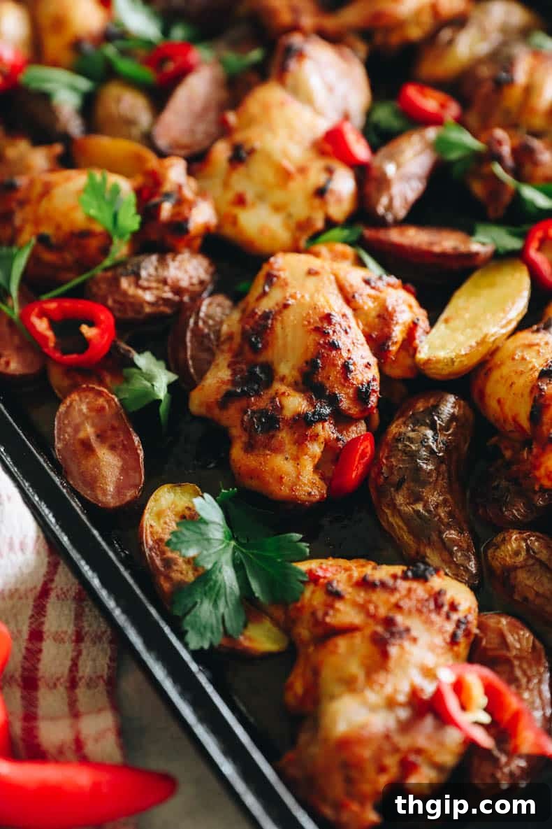 Sheet pan peri peri chicken thighs and roasted potatoes, garnished with fresh parsley.