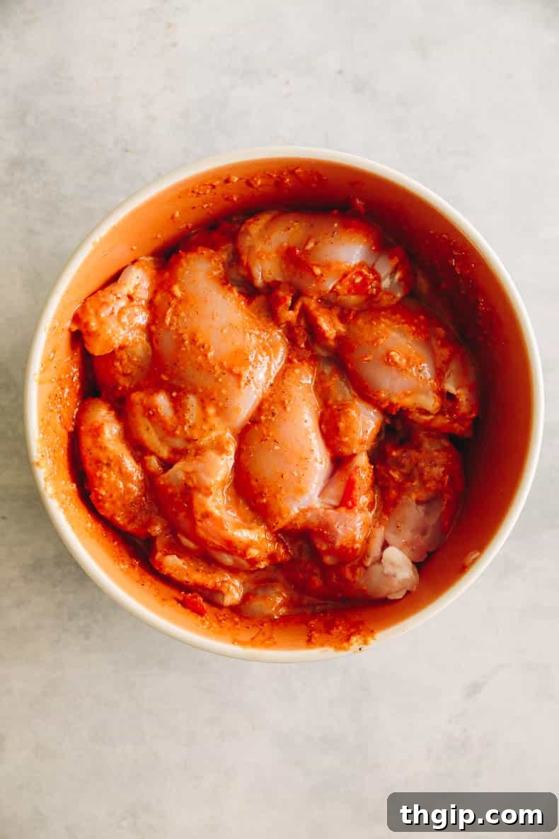Marinated peri peri chicken thighs in an orange bowl, ready for cooking.