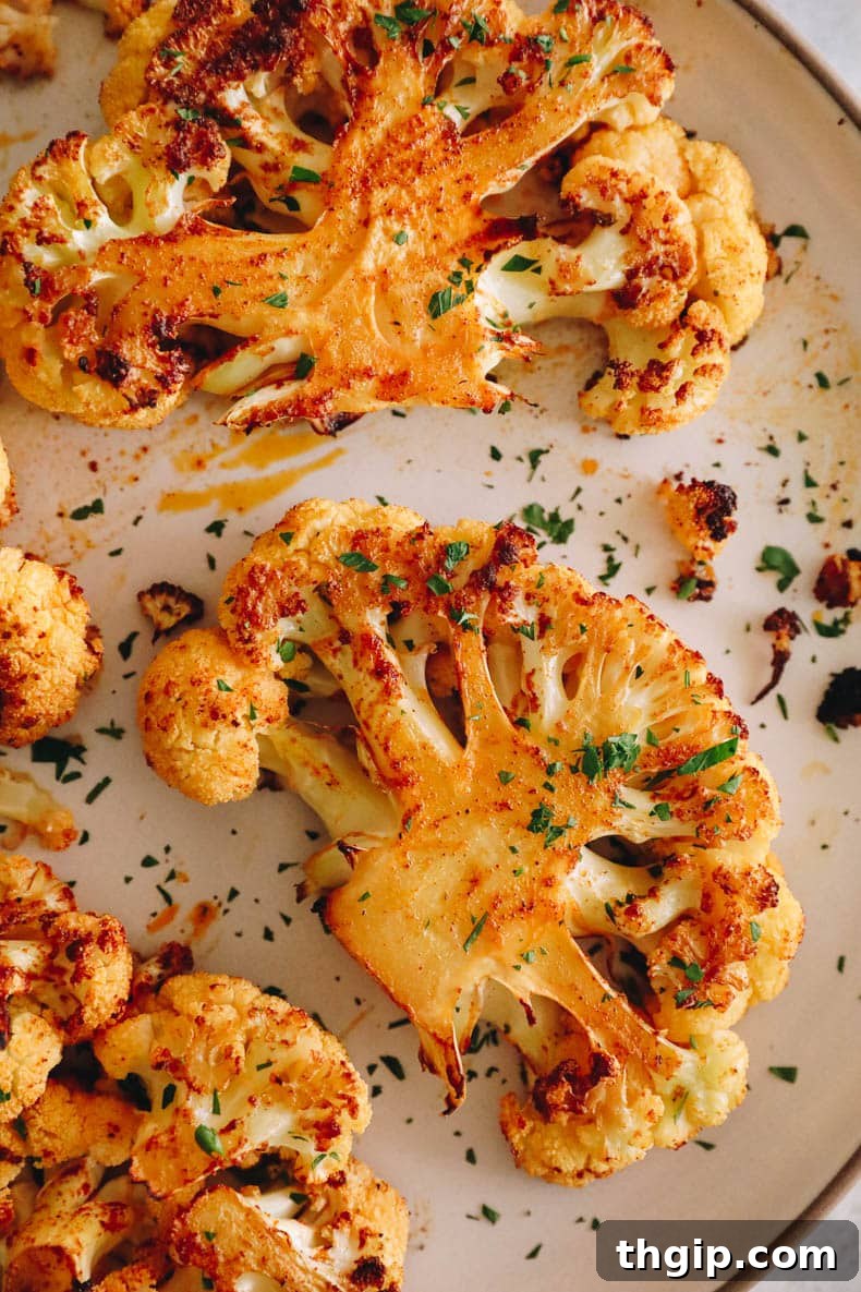 Golden Roasted Cauliflower Steaks 2 Crispy roasted cauliflower steak recipe on a white plate, garnished with fresh chopped parsley.