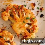 A close-up of a cauliflower steak recipe on a white plate, garnished with fresh chopped parsley.
