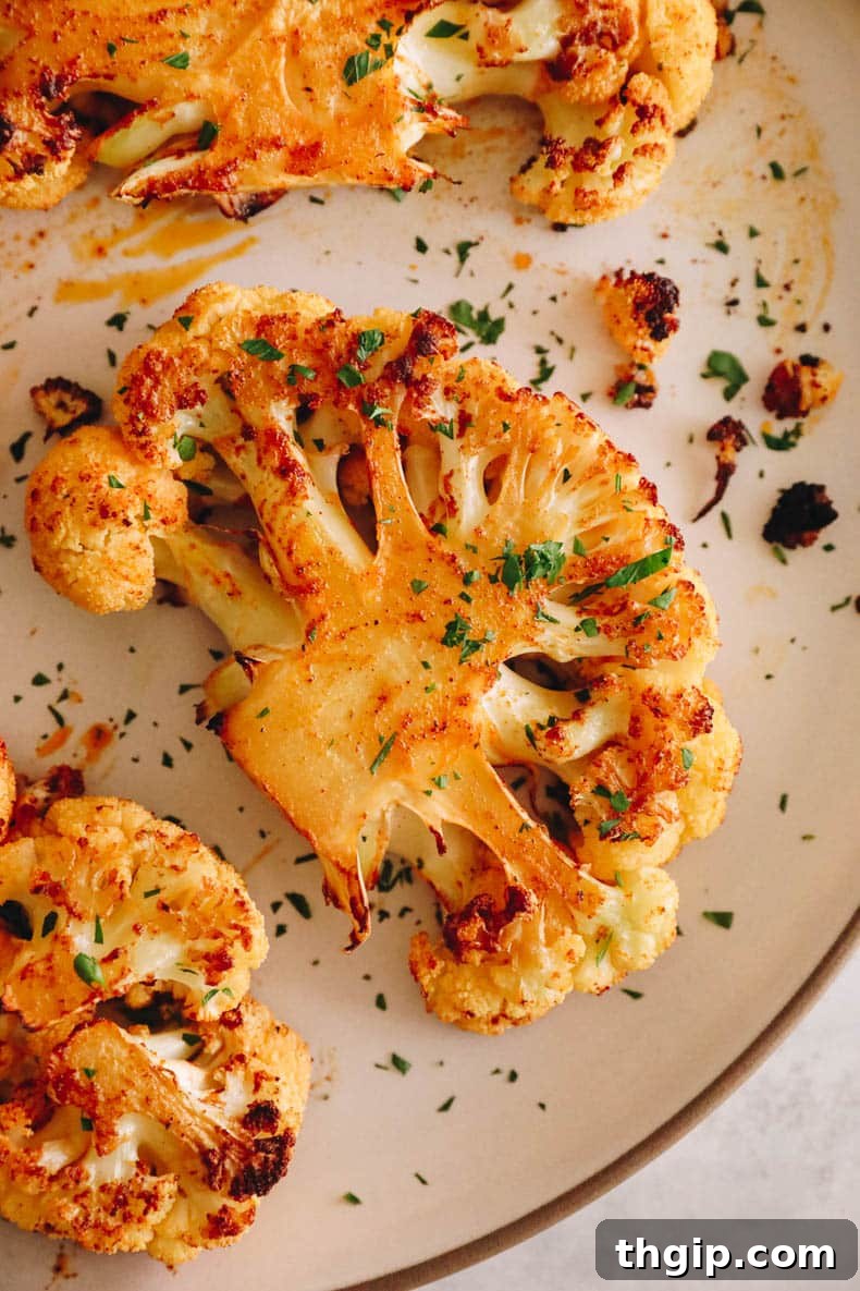 Golden Roasted Cauliflower Steaks 9 Upclose overhead image of a perfectly roasted cauliflower steak on a white plate, garnished with fresh chopped parsley.