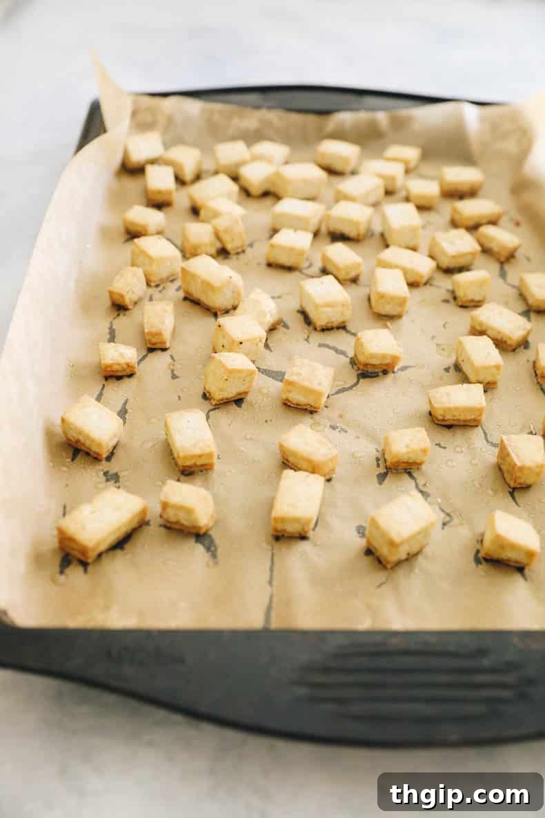 Cubed and roasted tofu pieces arranged on a parchment-lined baking sheet.
