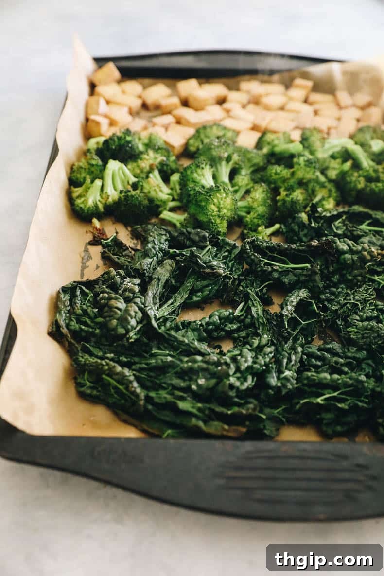 A sheet pan filled with roasted kale, tender broccoli florets, and crispy tofu cubes, freshly baked.