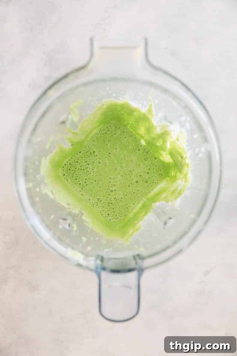 Creamy green goddess dressing being blended in a blender, showing its vibrant color.