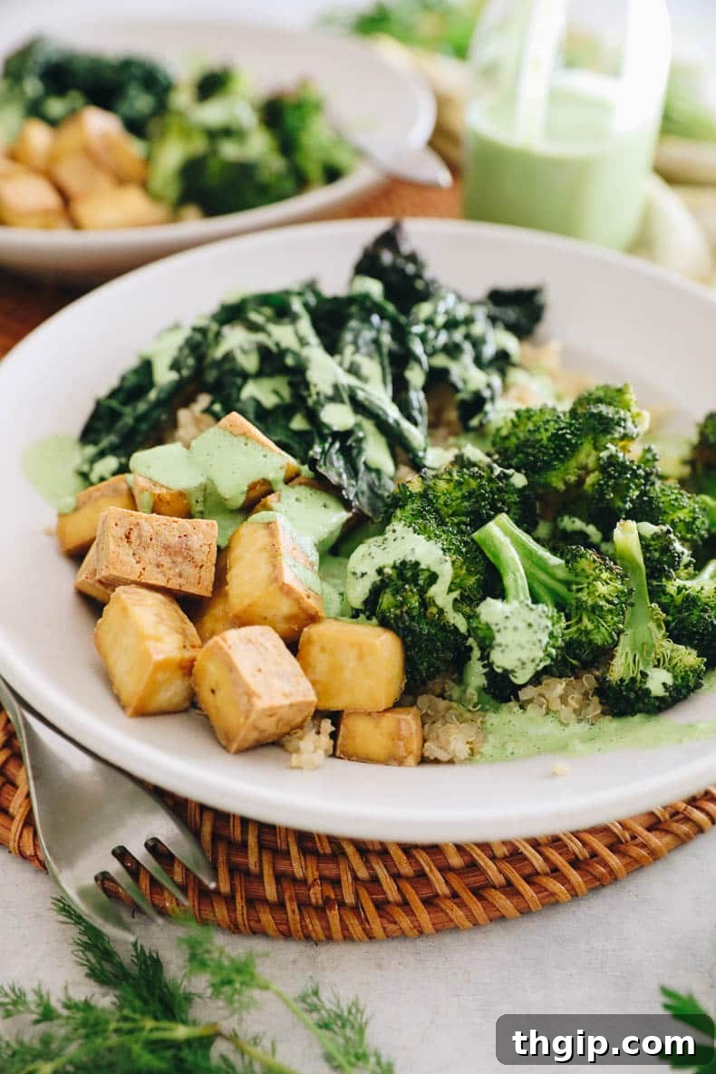 A beautifully assembled Green Goddess Tofu Bowl with quinoa, broccoli, kale, and tofu, generously drizzled with dressing.