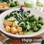 A beautifully assembled Green Goddess Tofu Bowl with quinoa, broccoli, kale, and tofu, generously drizzled with dressing.