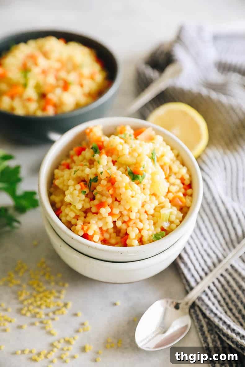 A bowl of pastina soup with carrots, celery, and onion, garnished with fresh parmesan, a lemon wedge, and parsley.