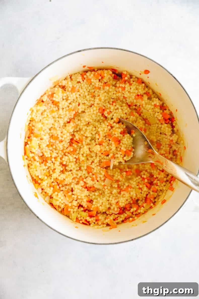 Pastina soup simmering in a large white Dutch oven, with small pasta absorbing the broth.