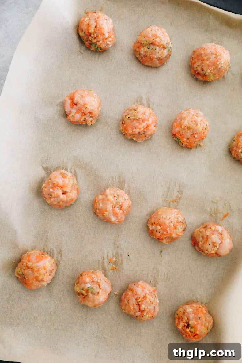 Kid-Approved Baked Chicken Meatballs with Secret Veggies 4 Raw chicken meatballs, perfectly rolled and arranged on a parchment-lined baking sheet.