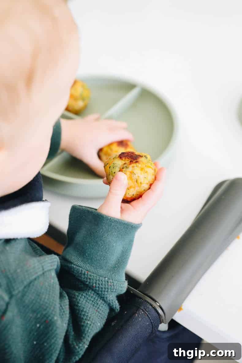 Kid-Approved Baked Chicken Meatballs with Secret Veggies 6 A baby joyfully holding a baked chicken meatball, demonstrating its kid-friendly appeal.