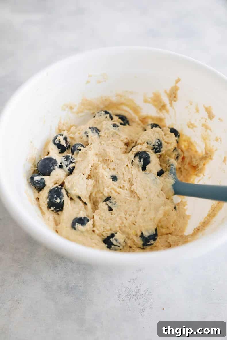 Zesty Lemon Blueberry Muffins 3 Lemon blueberry muffin batter in a white mixing bowl, showing the vibrant blueberries folded in.