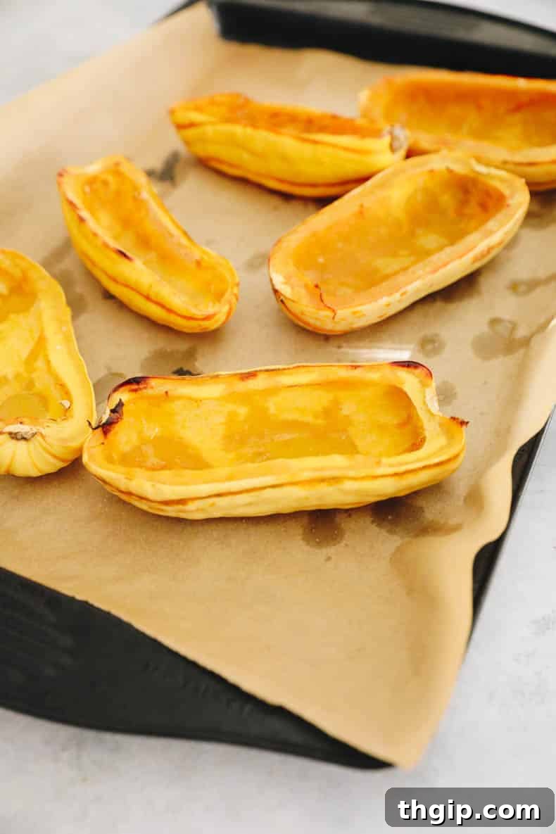 Hearty Farro-Filled Delicata Squash 4 Roasted delicata squash halves, golden brown and tender, on a baking sheet with parchment paper.