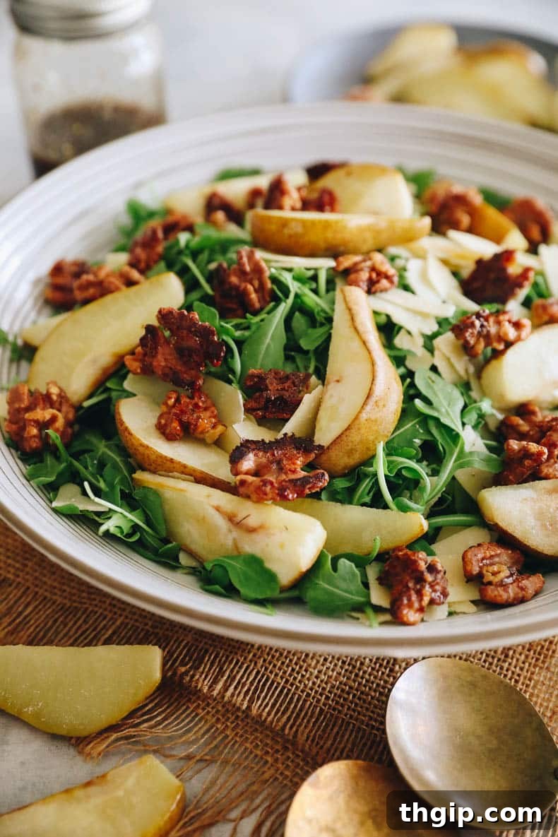 Caramelized Pear and Arugula Salad with Candied Walnuts 2 Roasted pear salad beautifully arranged over a bed of fresh arugula, garnished with crunchy candied walnuts, and delicate shaved parmesan, all glistening with balsamic vinaigrette in a large white salad bowl.