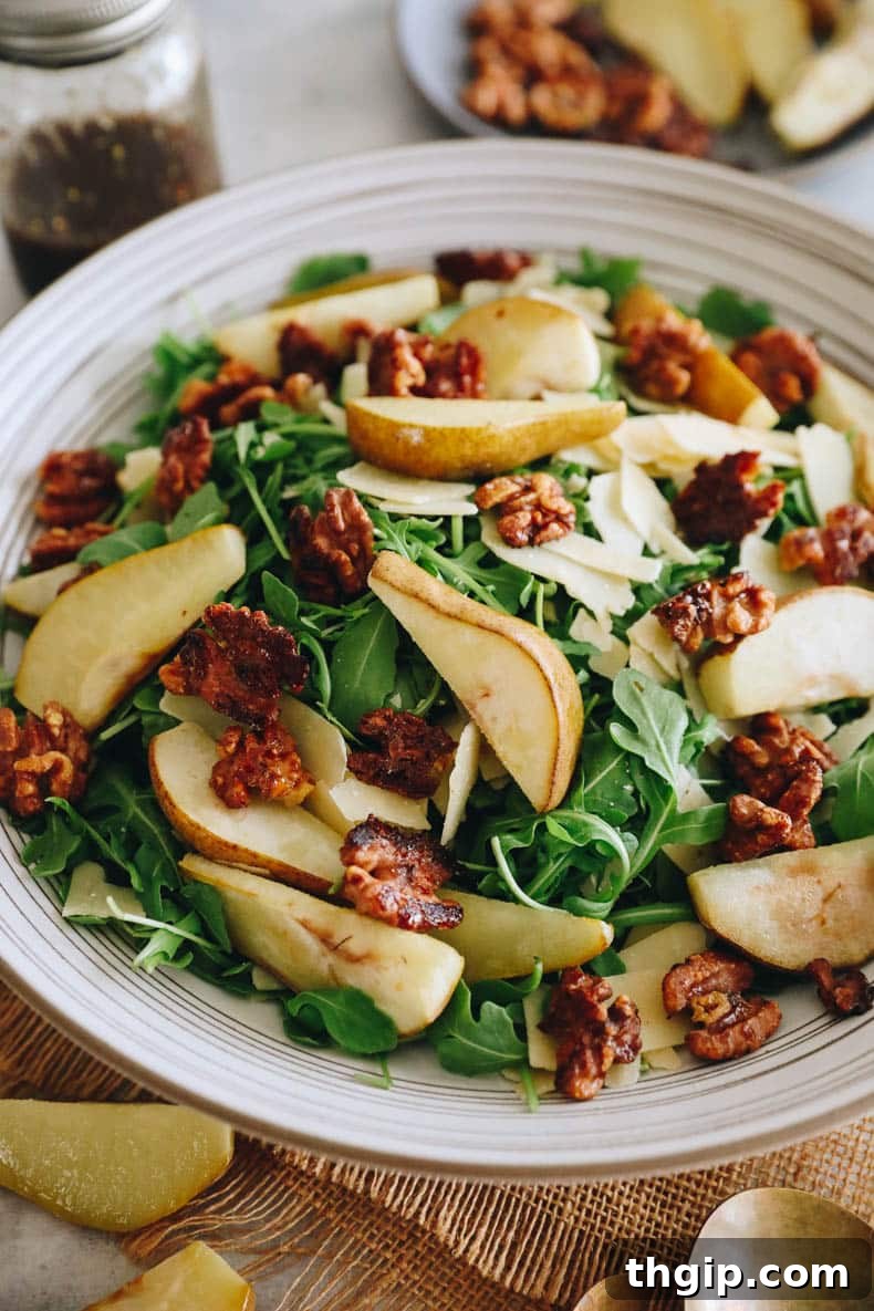Caramelized Pear and Arugula Salad with Candied Walnuts 6 A fully assembled roasted pear salad in a large white bowl, featuring a base of arugula topped with golden roasted pears, candied walnuts, and elegantly shaved parmesan, lightly dressed with balsamic vinaigrette.