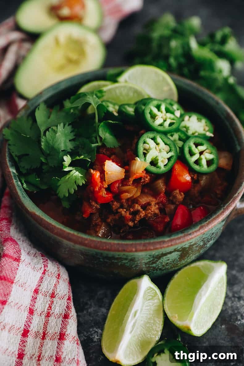 Texas-Style No-Bean Chili 2 A vibrant bowl of no-bean chili, garnished with fresh sliced jalapeño, bright lime wedges, and fragrant cilantro.
