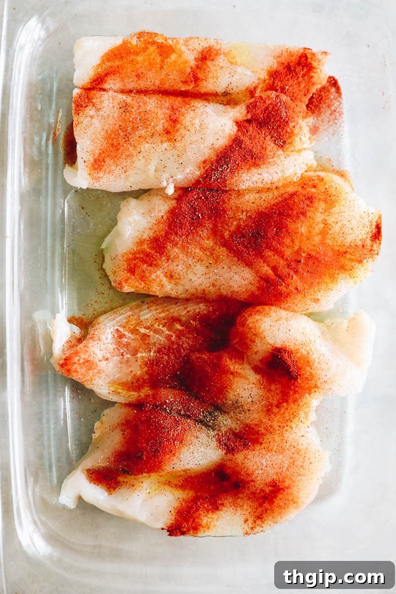 Lemon Herb Sheet Pan Cod 3 Marinated cod fillets in a glass dish, seasoned with olive oil, paprika, salt, and pepper, ready for baking.