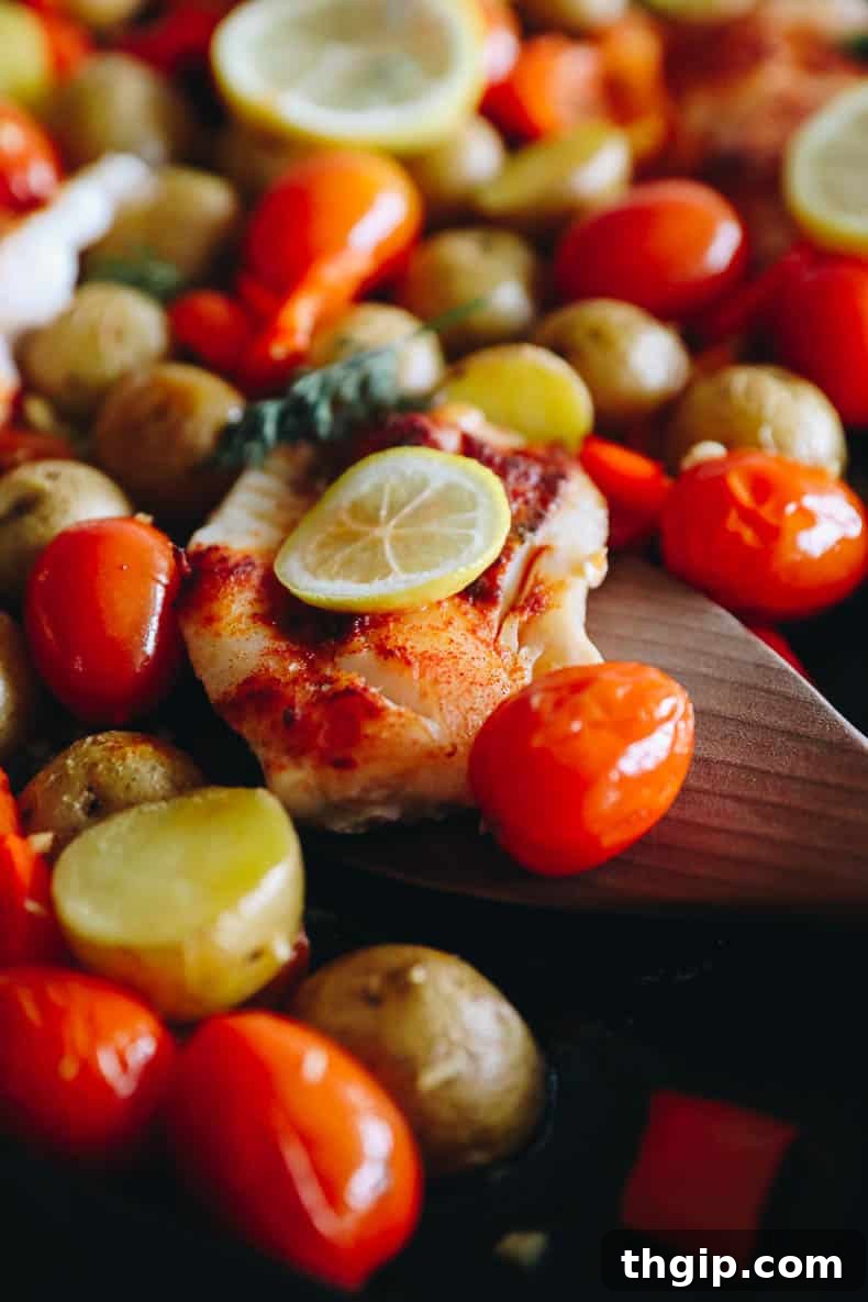 Lemon Herb Sheet Pan Cod 6 Close-up image of perfectly baked cod on a sheet pan, nestled among golden potatoes, vibrant bell peppers, and juicy cherry tomatoes.