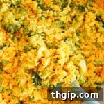 yellow curry rice with broccoli, peas and carrots in a caraway pot with a green spatula.