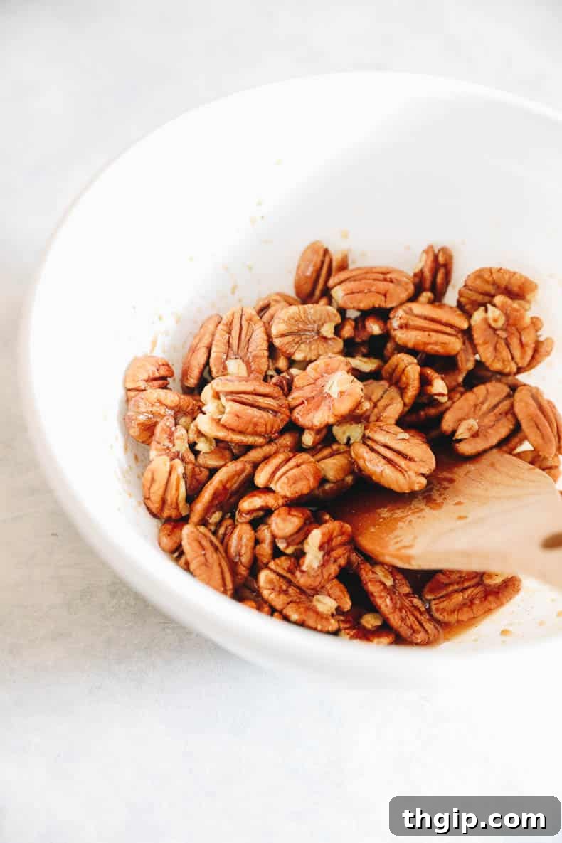 Candied Chili Pecans 3 Raw pecans in a mixing bowl, generously coated with a glistening maple syrup and spice mixture.