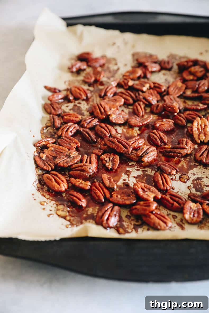 Candied Chili Pecans 4 Freshly roasted sweet and spicy pecans spread out on a parchment-lined baking sheet, cooling and hardening.