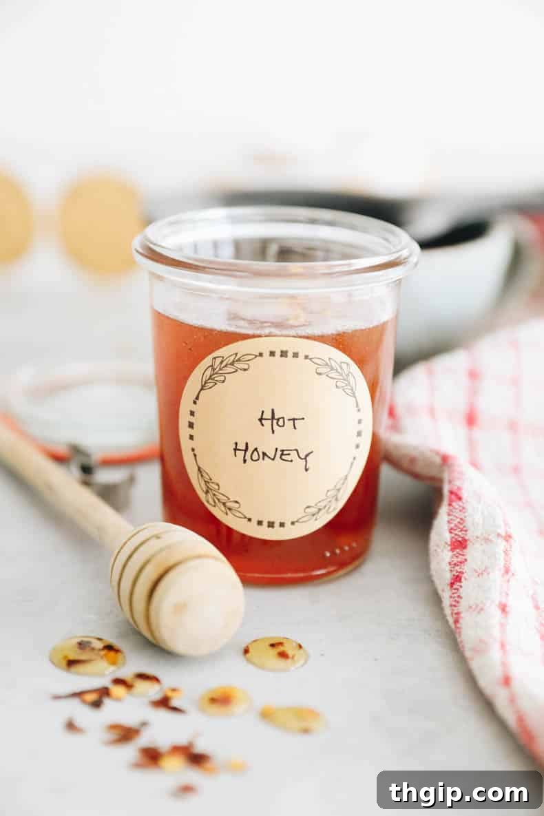 A small mason jar filled with golden hot honey, adorned with a rustic label, sits on a wooden surface.