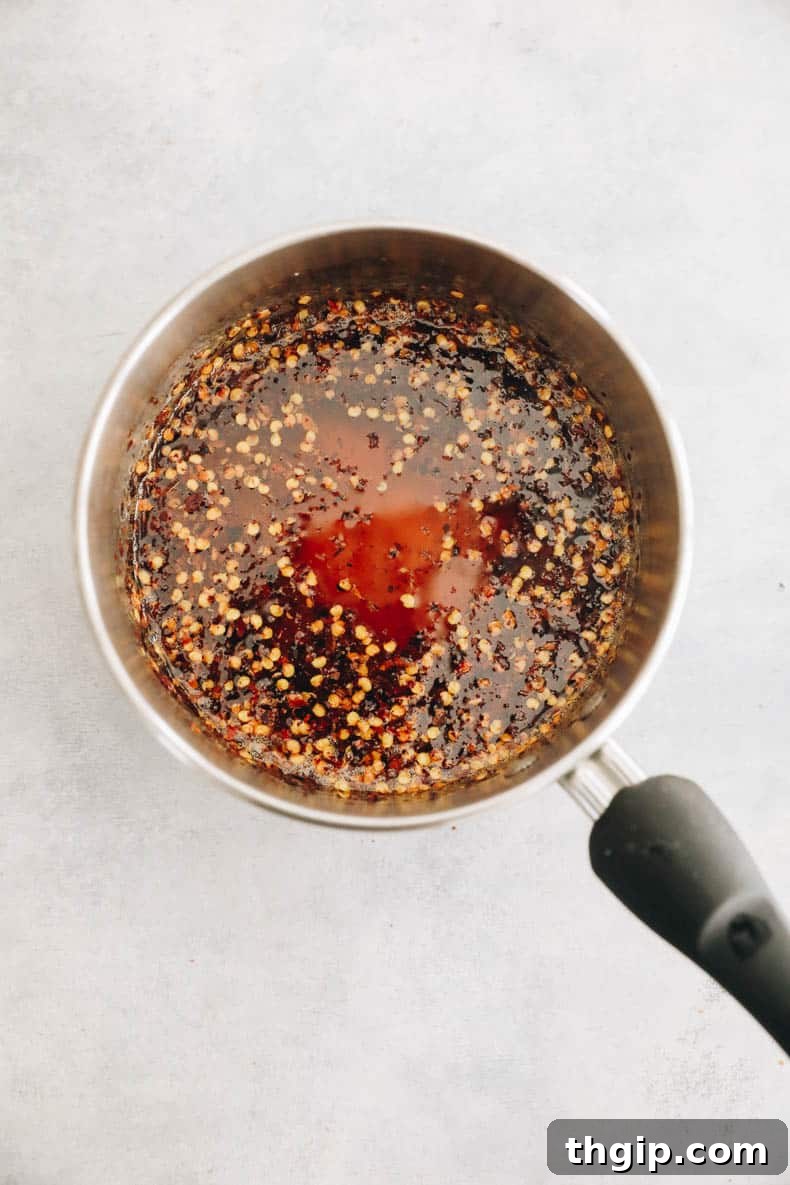 Golden honey bubbling gently in a saucepan with vibrant red chili flakes infusing their heat.