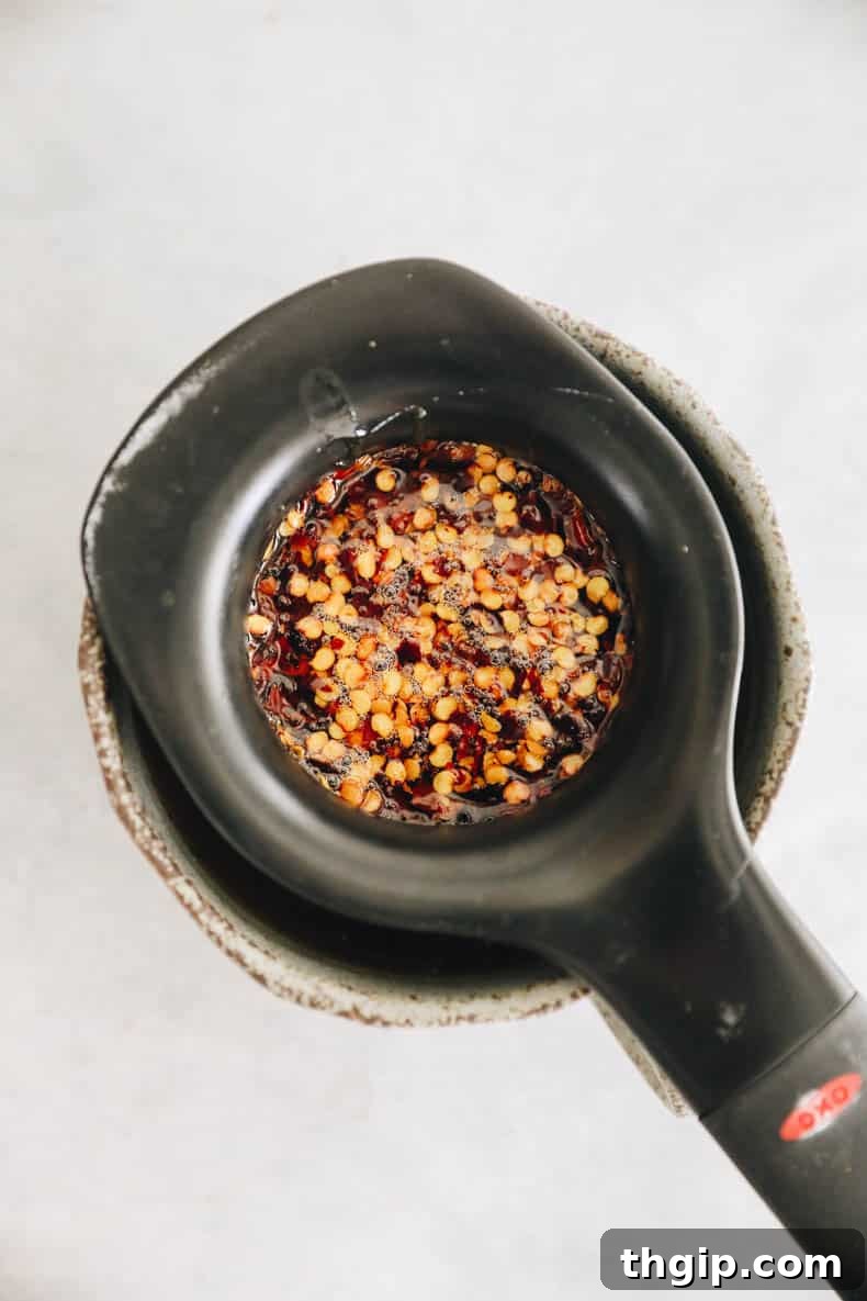 Infused hot honey being carefully strained through a fine-mesh sieve, separating the liquid from the red chili flakes.