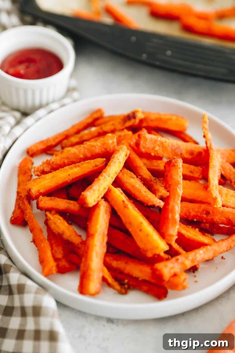 Golden Oven-Baked Carrot Sticks 2 crispy baked carrot fries on a white plate with ketchup, ready to be enjoyed.