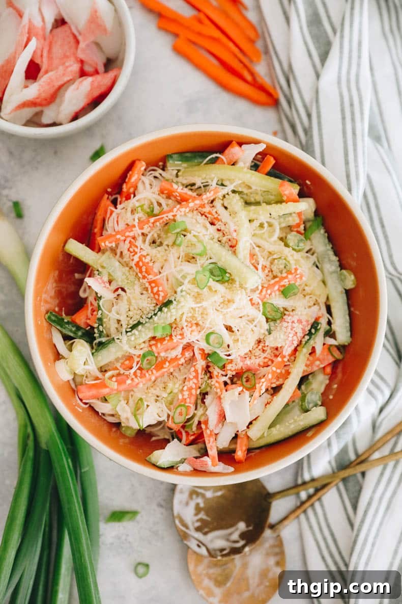 Creamy Spicy Crab Crunch 2 A vibrant Kani Salad served in a large orange bowl, showcasing shredded crab, julienned cucumbers and carrots, and a creamy dressing, garnished with sesame seeds.
