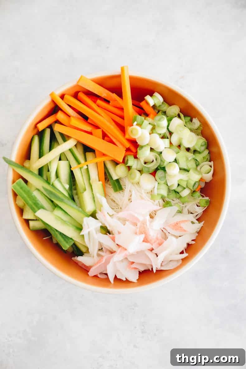 Creamy Spicy Crab Crunch 4 The vibrant salad base of Kani Salad, featuring shredded crab, crisp cucumber, and bright carrots, tossed together in a large orange bowl.