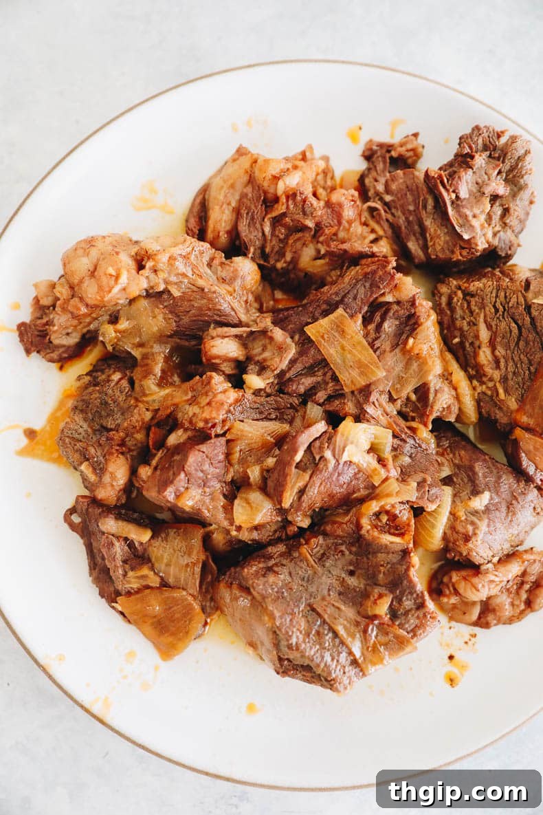 Tender chuck roast cooked and resting on a white plate, ready to be shredded or sliced.