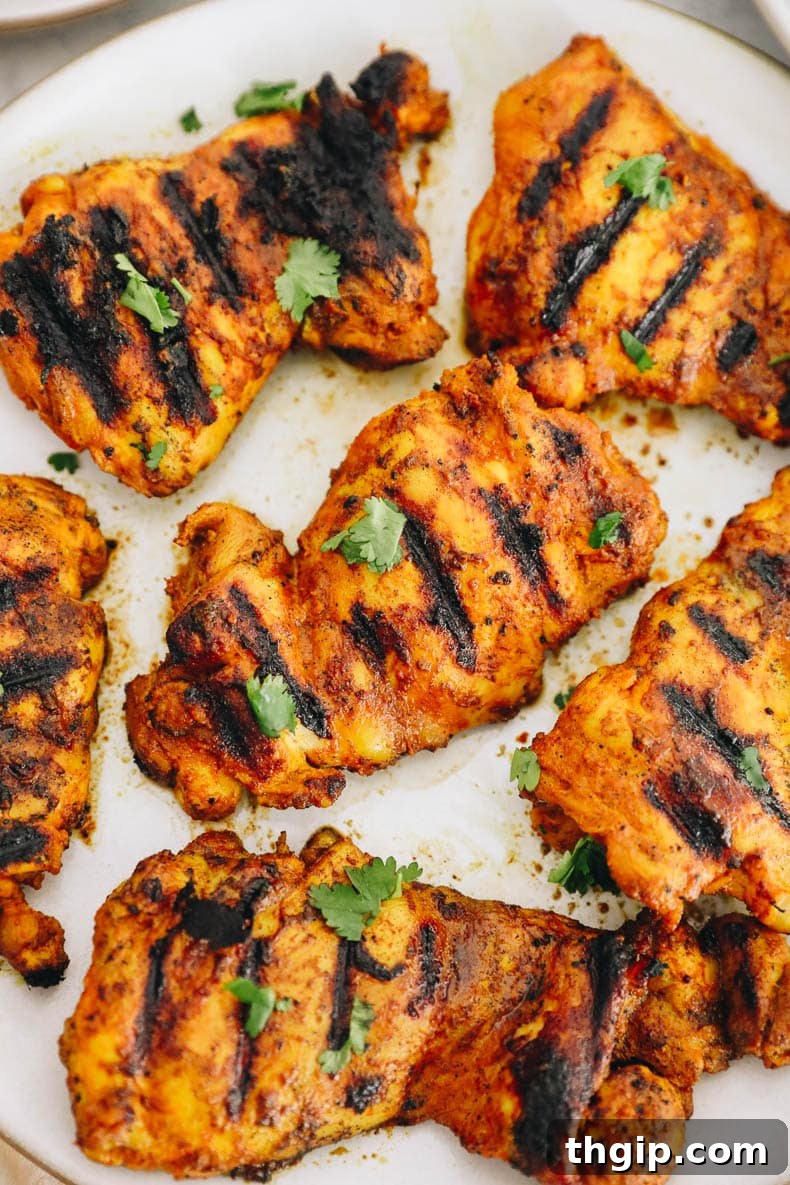 Close-up of grilled turmeric chicken on a white plate, showing the vibrant color and juicy texture.