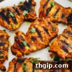 close-up of grilled turmeric chicken on a white plate and sprinkled with cilantro.