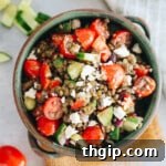 Hearty lentil salad with tomatoes, peppers, cucumber and feta in a large green serving bowl.