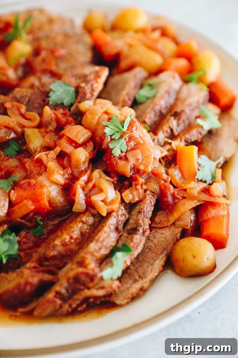 Perfectly Tender Smoked Brisket 2 A beautifully cooked Jewish brisket recipe, served on a white platter with caramelized onions, tender carrots, roasted baby potatoes, and a sprinkle of fresh parsley.