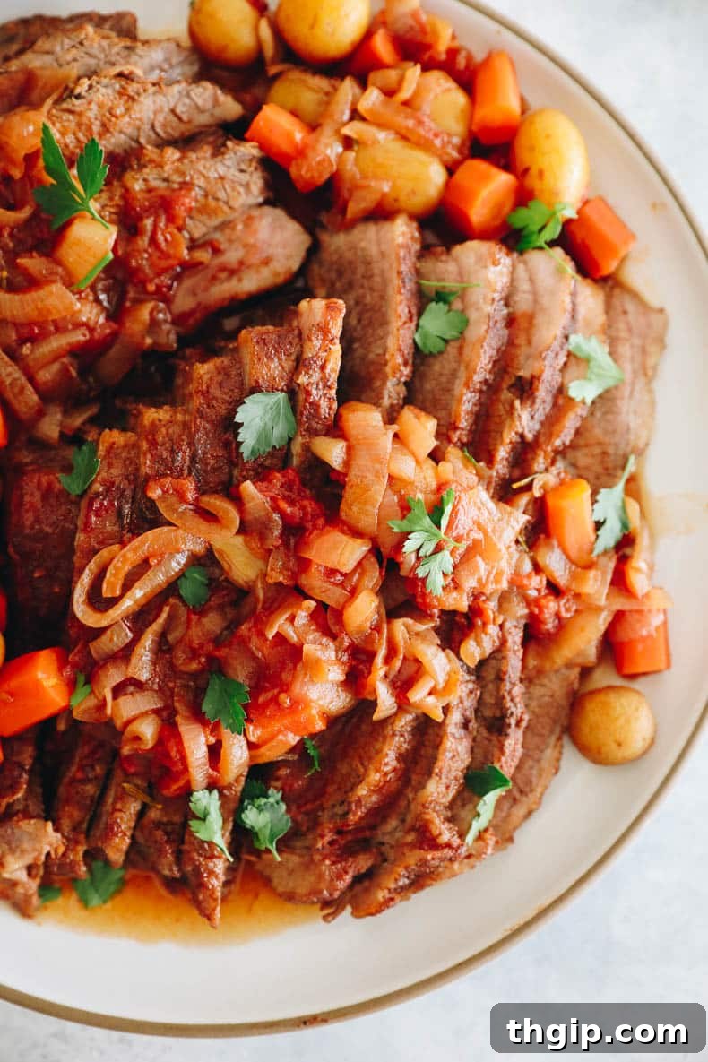 Perfectly Tender Smoked Brisket 12 Overhead shot of a delicious brisket with caramelized onions, tender roasted potatoes, and sweet carrots, glistening in its rich sauce on a white platter.