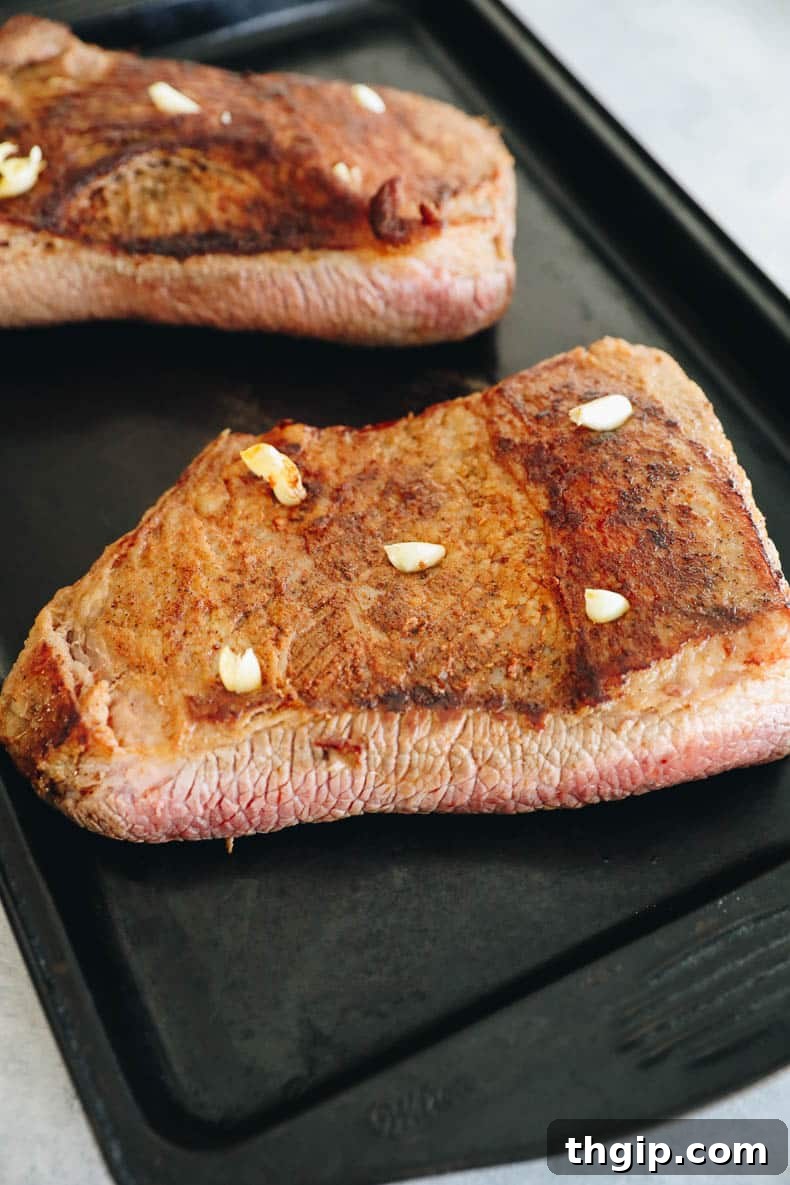 Perfectly Tender Smoked Brisket 5 Close-up of a seared brisket with small cuts, each containing a whole garlic clove, ready for braising.
