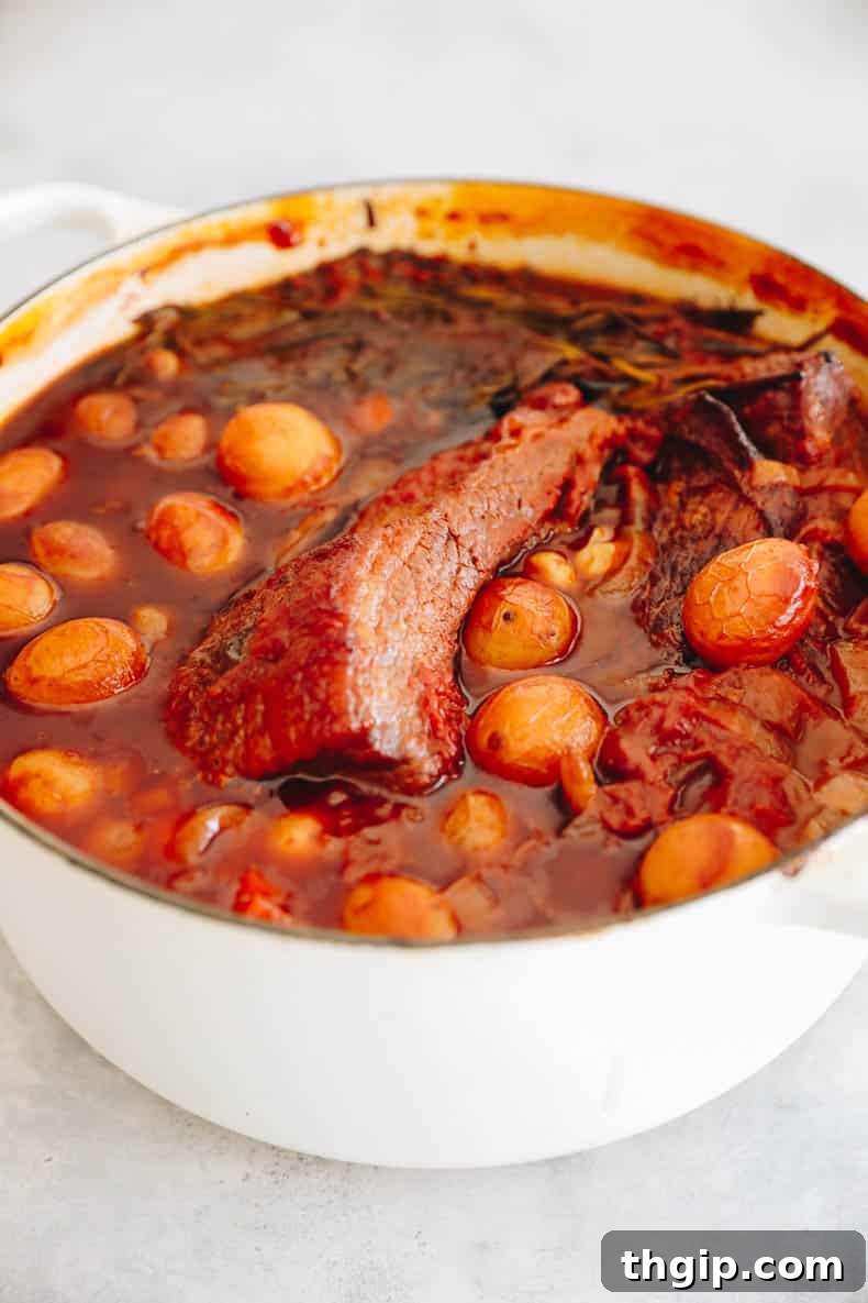 Perfectly Tender Smoked Brisket 8 A Dutch oven filled with seared brisket submerged in rich sauce, topped with carrots, potatoes, and fresh herbs, ready for slow cooking in the oven.